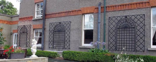Treillage Metal Wall Trellises installed between the windows of a house with a grey façade