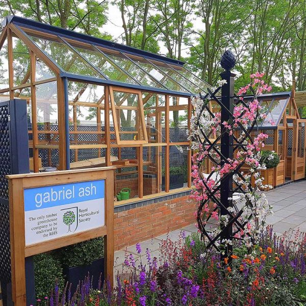 The Charleston Rose Obelisk by Classic Garden Elements in front of a Gabriel Ash greenhouse