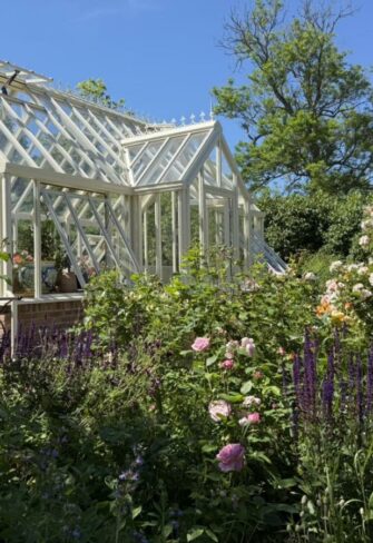 A striking classic English greenhouse in pristine white, perfectly contrasted by a sleek black trellis obelisk. This elegant garden feature blends timeless design with modern style — ideal for refined garden landscapes