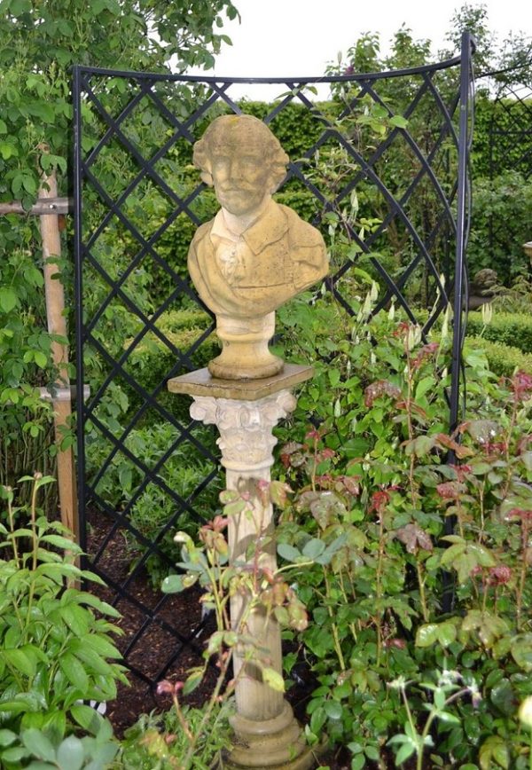 Exedra Garden Obelisk framing a Shakespeare bust displayed atop a stone pillar in a garden in spring
