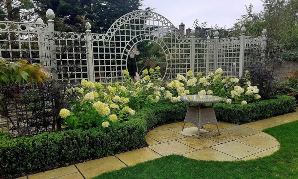 The Trianon Rose Treillage Set by Classic Garden Elements behind a border of hydrangeas and a box hedge