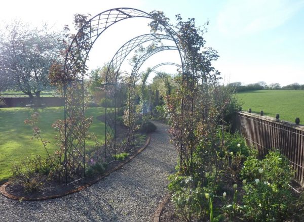 Bagatelle Round-Top Garden Arches by Classic Garden Elements creating a beautiful floral walkway in a spring garden