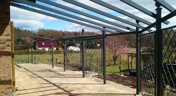 A bespoke Piemont Metal Pergola by Classic Garden Elements with side trellis panels