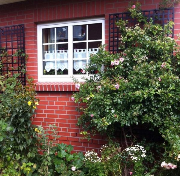 Two metal wall trellises by Classic Garden Elements on a brick house wall, covered in roses